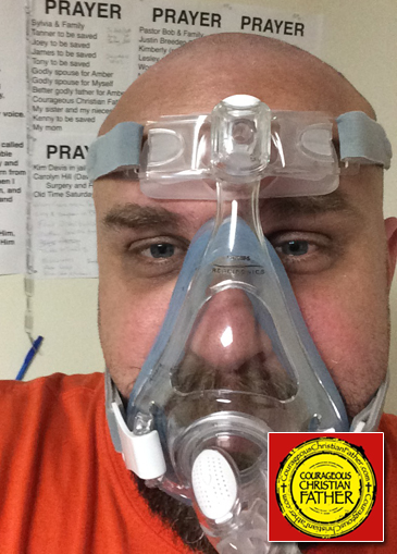 Steve wearing a CPAP mask. With his Prayer Wall showing in the background.
